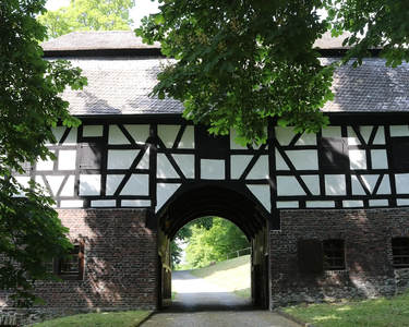 Historisches Fachwerk-Torhaus in Wehbach im Siegerland mit gemauertem Sockel, schwarzem Gebälk und Durchfahrtstor, umgeben von Bäumen und Natur