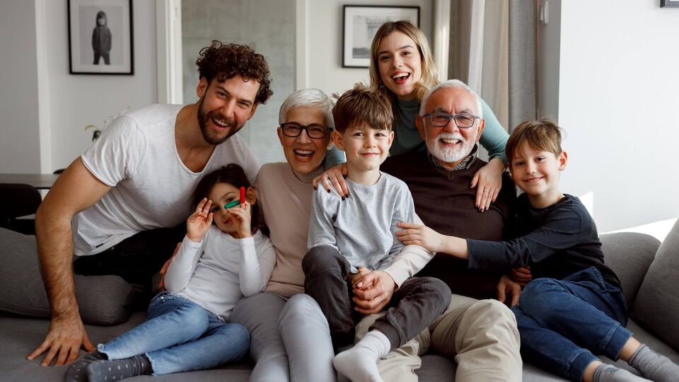 Mehrgenerationenfamilie sitzt gemeinsam auf einem Sofa und lächelt